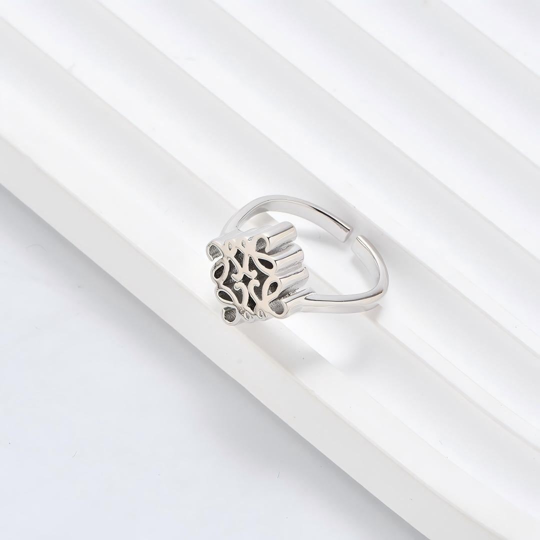 Clean, angled shot of the ring on a finger or stand, showcasing the square silhouette and intricate hollow pattern against a solid background.