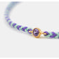 Bracelet with purple and green braided design and a gold clasp with a purple gemstone on a white background.