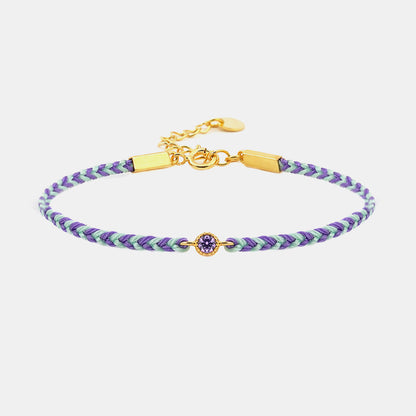 Braided bracelet with purple and green pattern and gold clasp on a white background