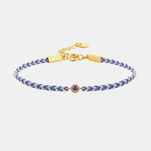 Braided bracelet with purple and green pattern and gold clasp on a white background