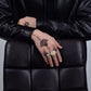 Person wearing a black leather jacket with visible tattoos on their hands and fingers.