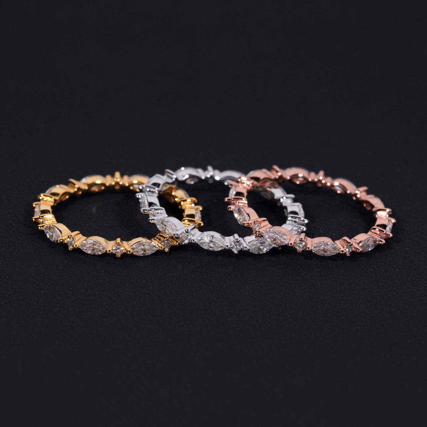Three diamond bracelets in gold, silver, and rose gold on a black background