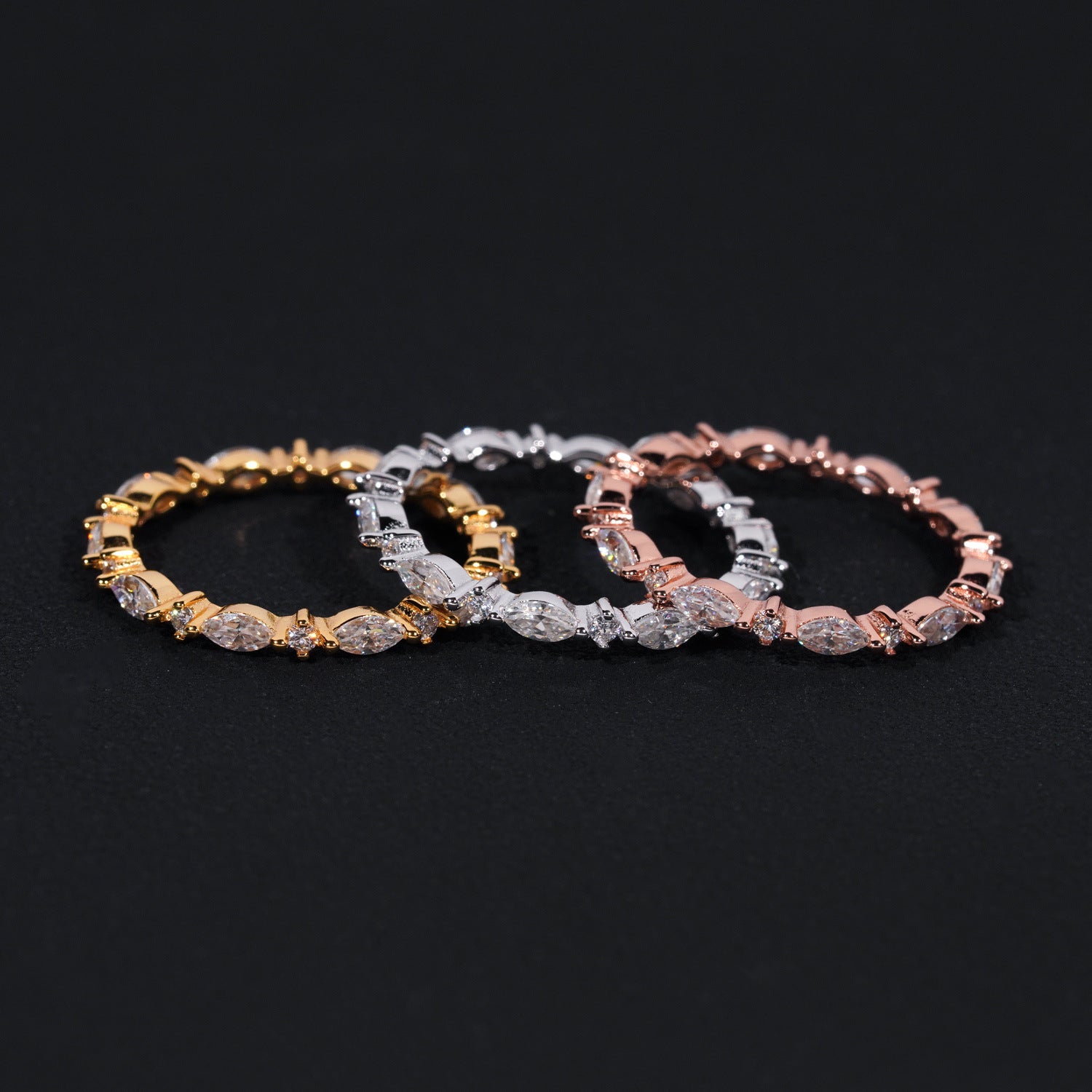 Three diamond bracelets in gold, silver, and rose gold on a black background