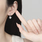 Heart-shaped earring being worn and held by a hand against a neutral background