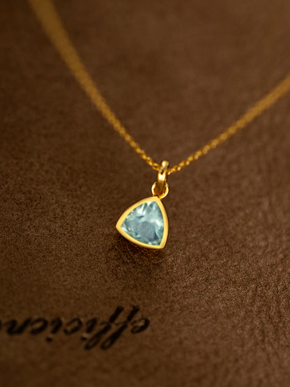 Gold necklace with a blue gemstone pendant on a brown textured background