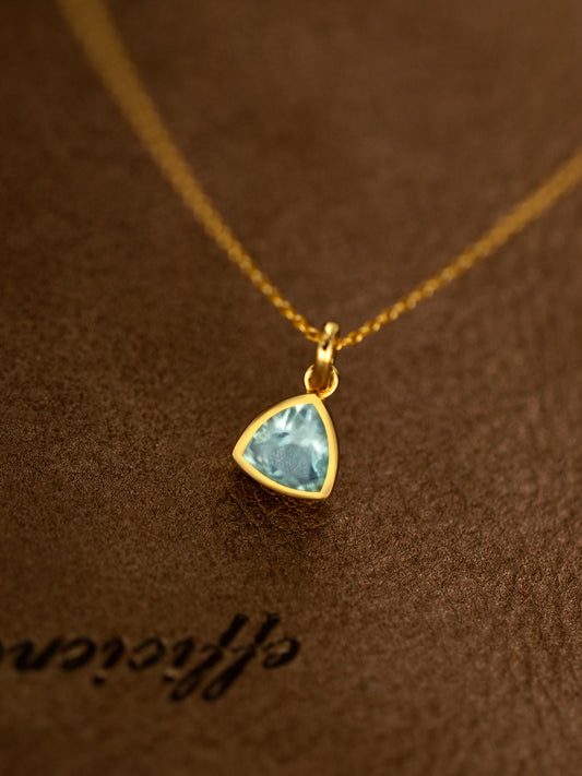 Gold necklace with a blue gemstone pendant on a brown textured background