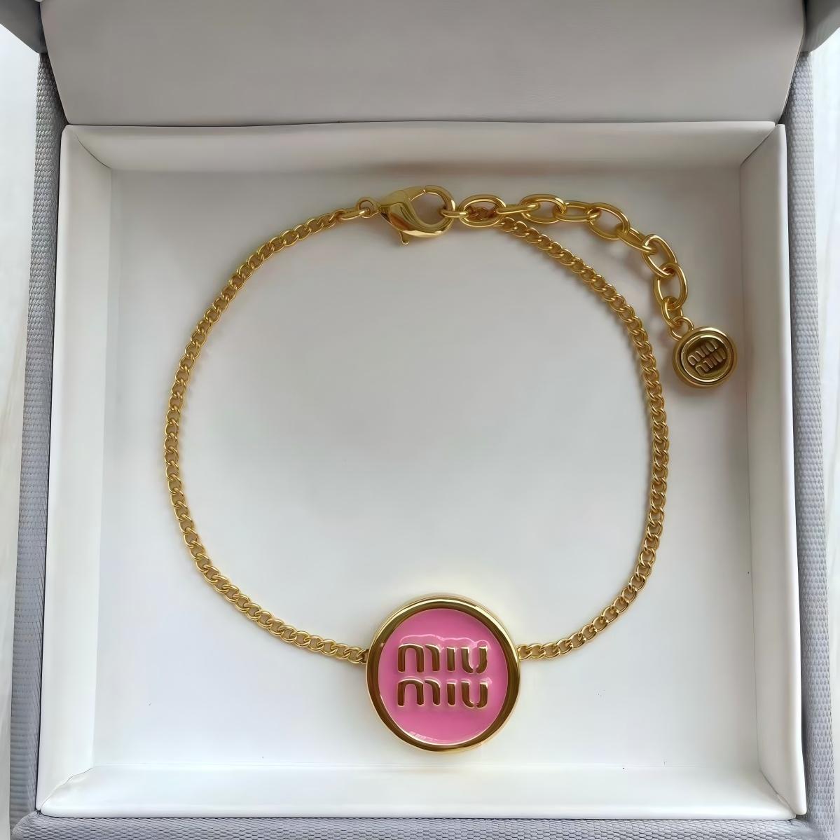 The bracelet arranged artistically on a textured neutral surface (like grey felt or marble), capturing its full shape and the dramatic contrast of materials. Alt text: "Miu Miu Gold-Tone Metal and Black Enamel Designer Cuff Bracelet."