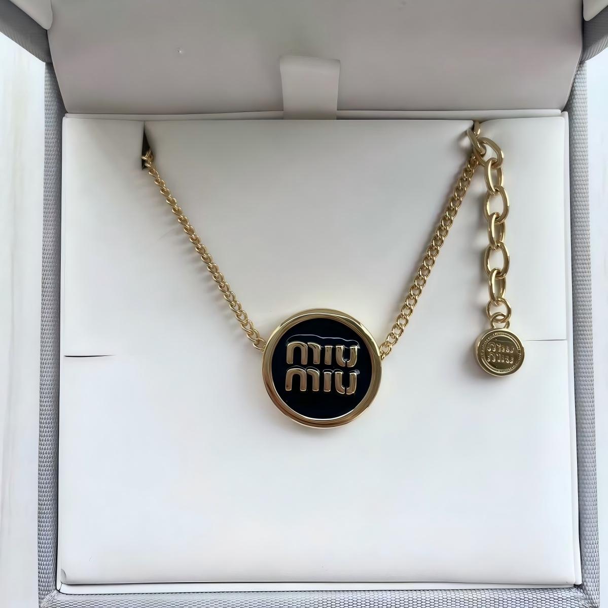 The bracelet arranged artistically on a textured neutral surface (like grey felt or marble), capturing its full shape and the dramatic contrast of materials. Alt text: "Miu Miu Gold-Tone Metal and Black Enamel Designer Cuff Bracelet."