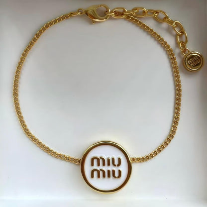 The bracelet arranged artistically on a textured neutral surface (like grey felt or marble), capturing its full shape and the dramatic contrast of materials. Alt text: "Miu Miu Gold-Tone Metal and Black Enamel Designer Cuff Bracelet."