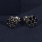 Pair of black and silver earrings on a dark blue fabric background