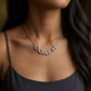A close-up of a woman wearing a silver-tone chain necklace with the word 'COACH' spelled out in sparkling letterstones, paired with a black camisole top.