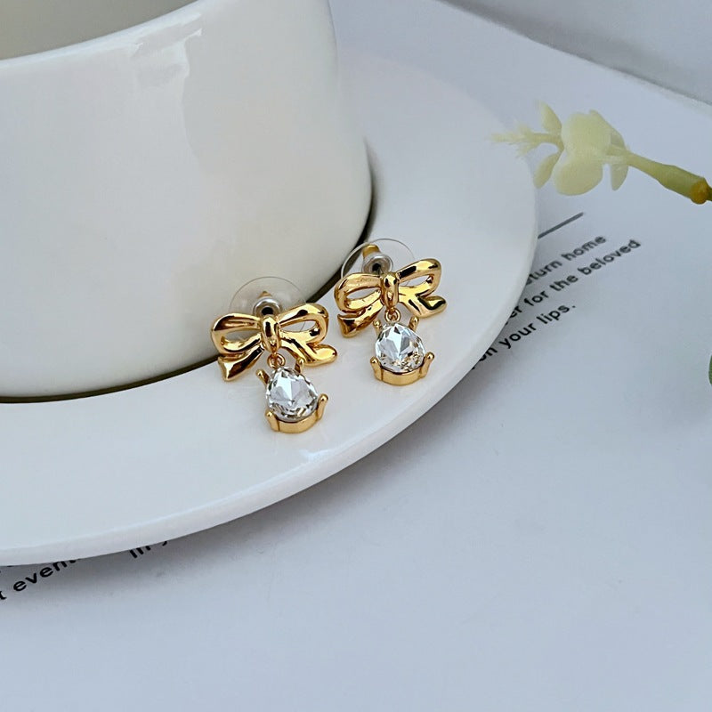 Earrings on a soft blush pink or cream background, showcasing the teardrop silhouette and delicate bow detail. Alt: “New Kate Spade Gold Dainty Tied Up Tear Drop Earrings – Feminine Bow Knot Jewelry.”
