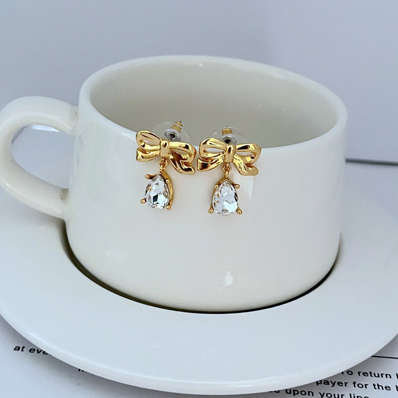  Earrings on a soft blush pink or cream background, showcasing the teardrop silhouette and delicate bow detail. Alt: “New Kate Spade Gold Dainty Tied Up Tear Drop Earrings – Feminine Bow Knot Jewelry.”