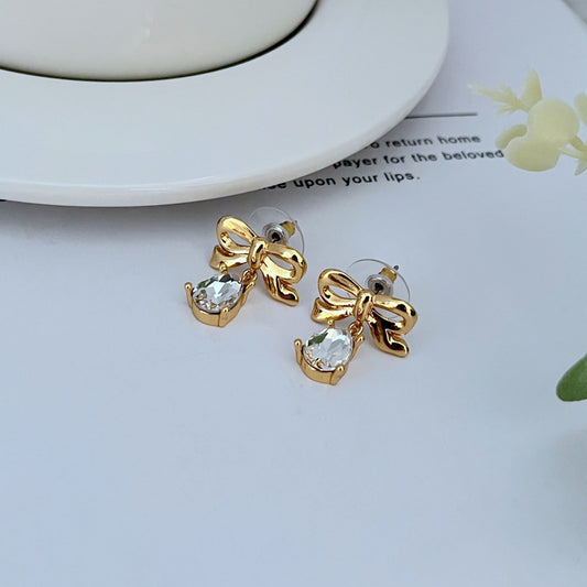: Earrings on a soft blush pink or cream background, showcasing the teardrop silhouette and delicate bow detail. Alt: “New Kate Spade Gold Dainty Tied Up Tear Drop Earrings – Feminine Bow Knot Jewelry.”