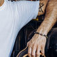 Person holding a steering wheel with tattoos on arm and wearing a bracelet.