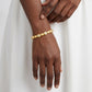 Macro shot of hands with bracelet, deep skin tone, white outfit background, soft light, minimal elegant style.