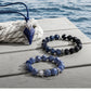Blue beaded necklace and bracelet on a wooden surface with water in the background
