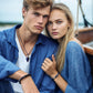 Two people sitting close together on a boat, wearing blue and white clothing.