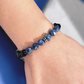 Close-up of a wrist wearing a blue beaded bracelet against a blue and gray background