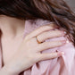 Close-up of a hand wearing a ring with pink fabric in the background