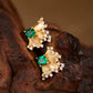 Gold earrings with emerald green gemstones on a wooden surface