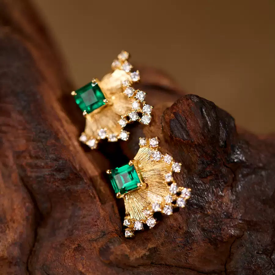 Gold earrings with emerald green gemstones on a wooden surface