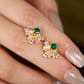 Gold earrings with green gemstones on a finger