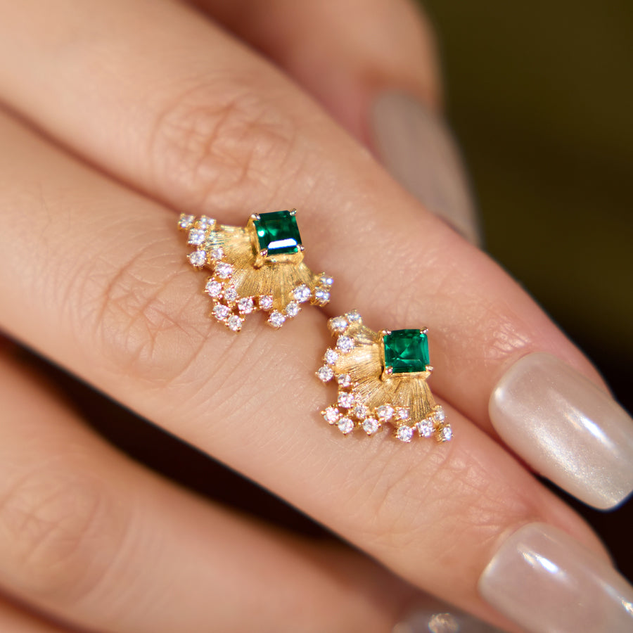 Gold earrings with green gemstones on a finger