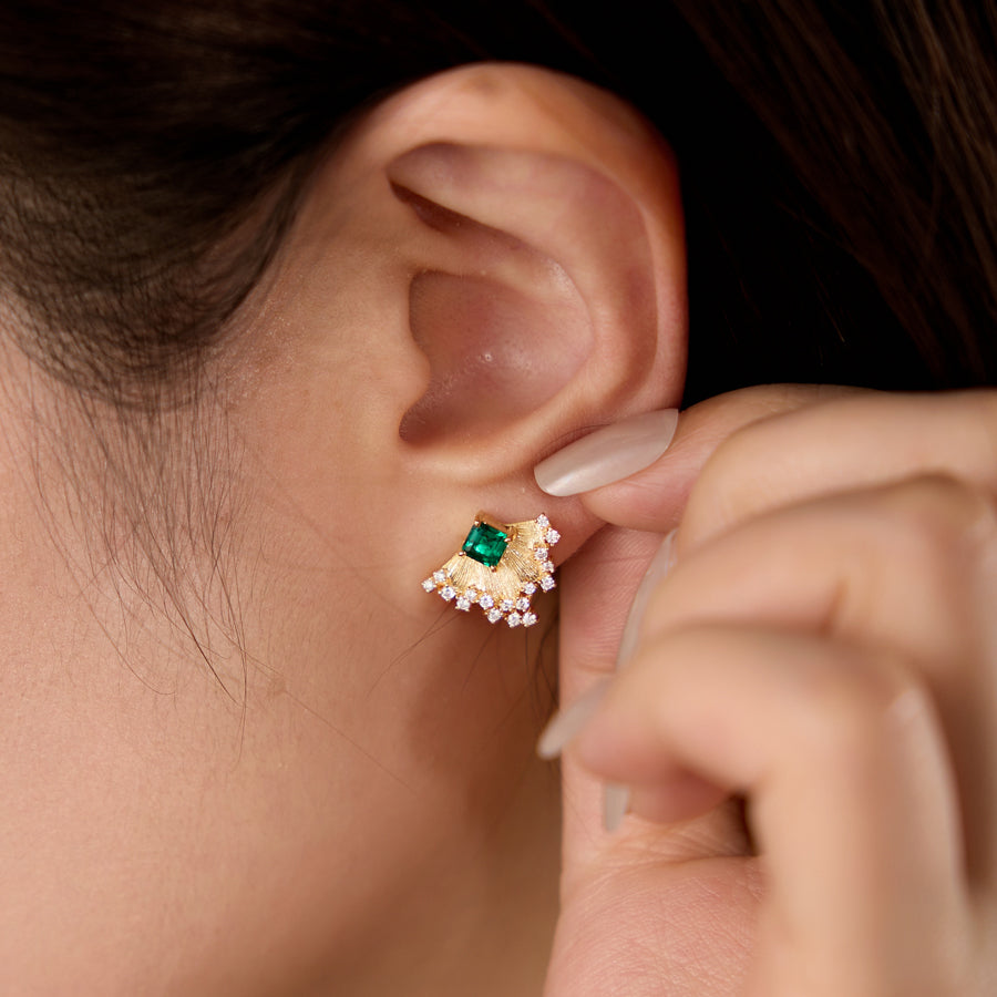 Close-up of an ear wearing a gold earring with a green gemstone.