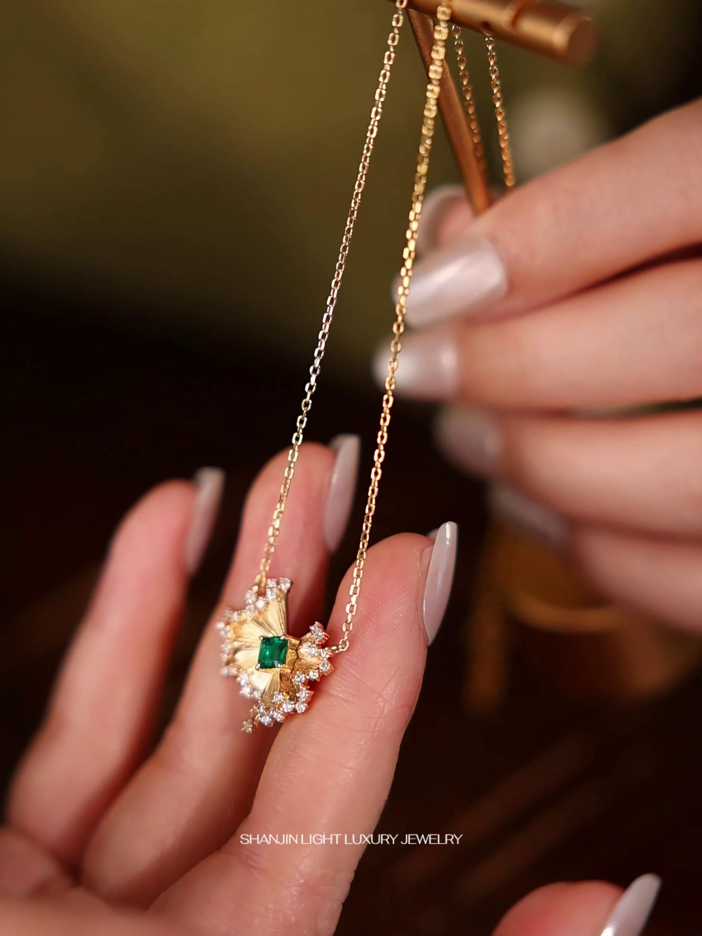 Gold necklace with a green gemstone held by a hand against a blurred background