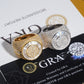 Two large statement ring bombers in yellow gold and silver, both heavily paved with clear stones, displayed on top of GRA branded cards.