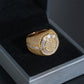 A gold signet ring with pave-set clear stones, displayed inside a black velvet-lined jewelry box.