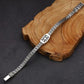 Silver bracelet with intricate design on a wooden block against a dark background
