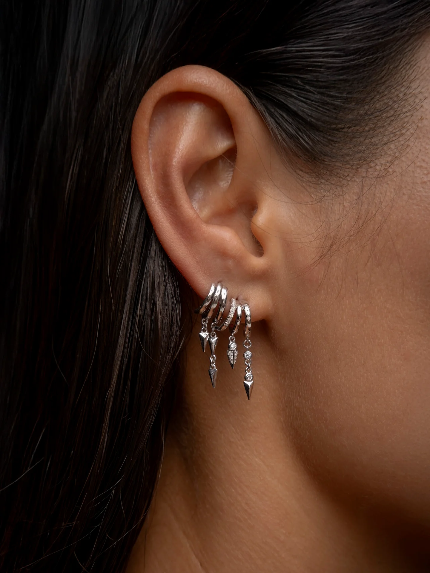 Close-up of an ear wearing silver S925 Sterling Silver Lynx Stacked Triple Hoop Huggie Illusion Earringshoop earrings with a blurred background