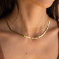 Close-up of a person wearing two gold necklaces on a plain background