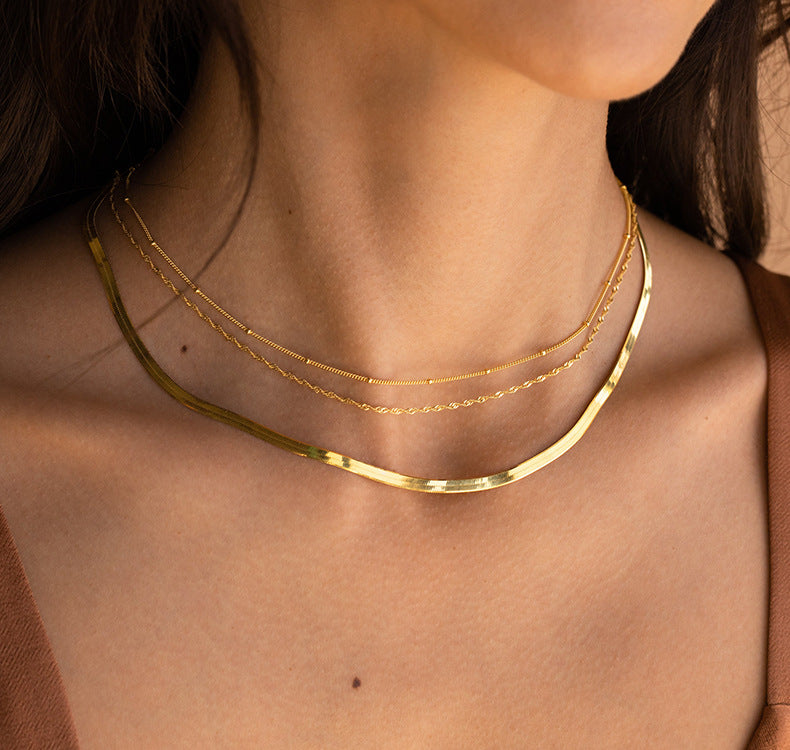 Close-up of a person wearing two gold necklaces on a plain background