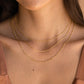 Close-up of a person wearing two gold necklaces on a neutral background