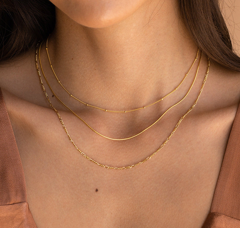 Close-up of a person wearing two gold necklaces on a neutral background