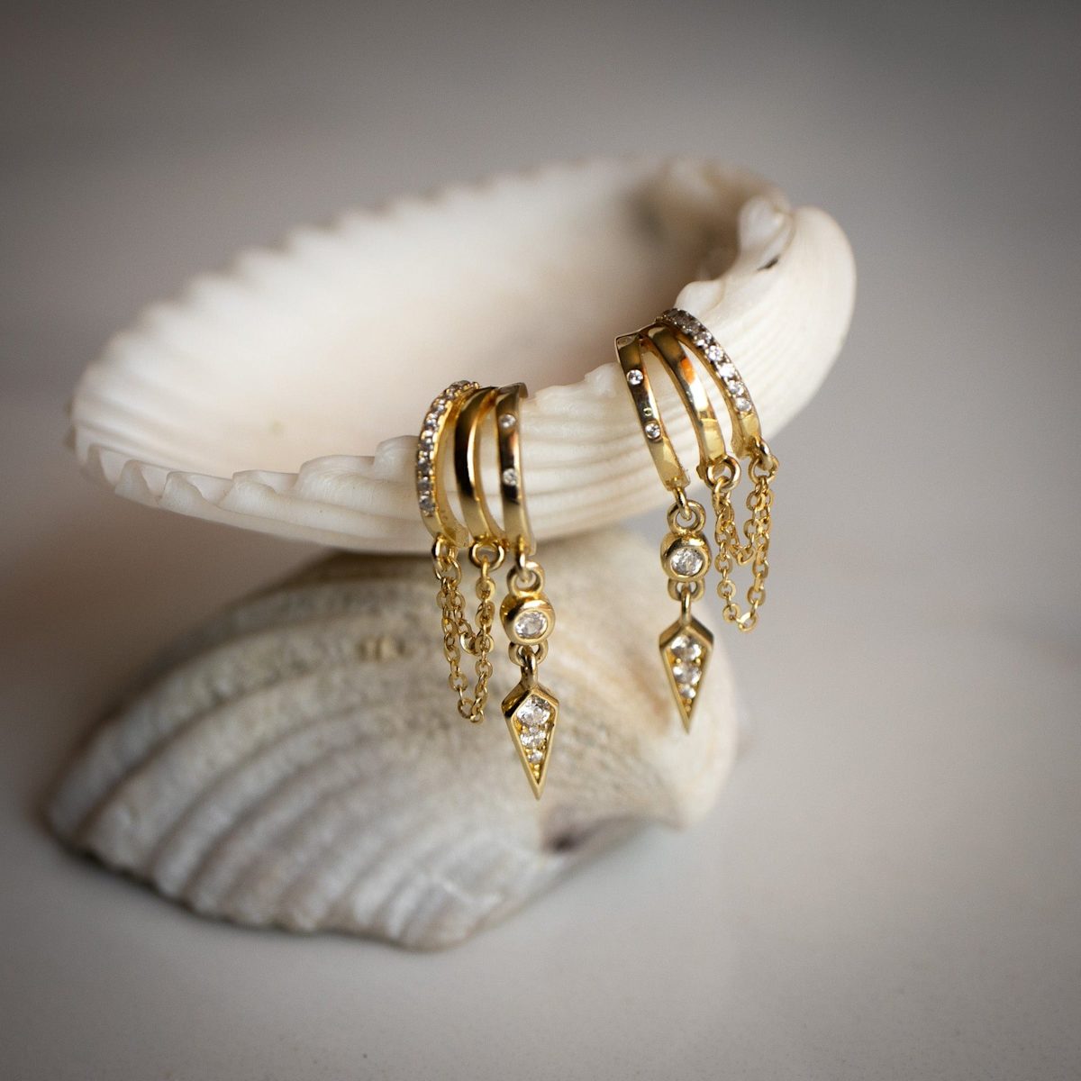 S925 Sterling Silver Palma Charm Earring hoop earrings with chains on a seashell against a neutral background