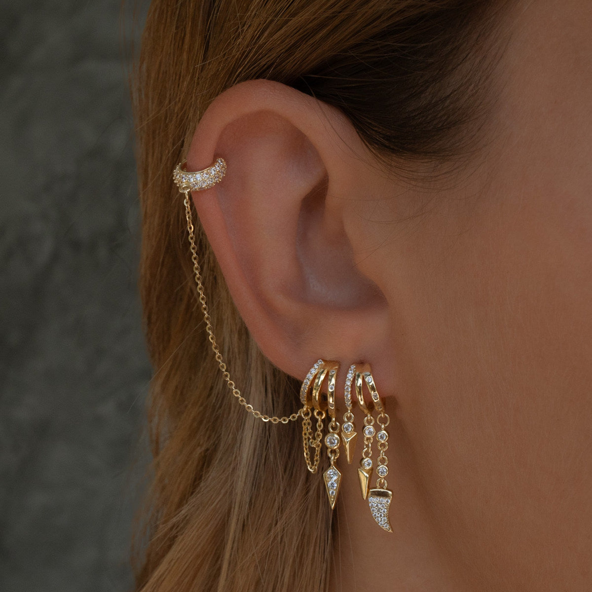 Close-up of an ear with S925 Sterling Silver Palma Charm Earring and a chain accessory against a neutral background