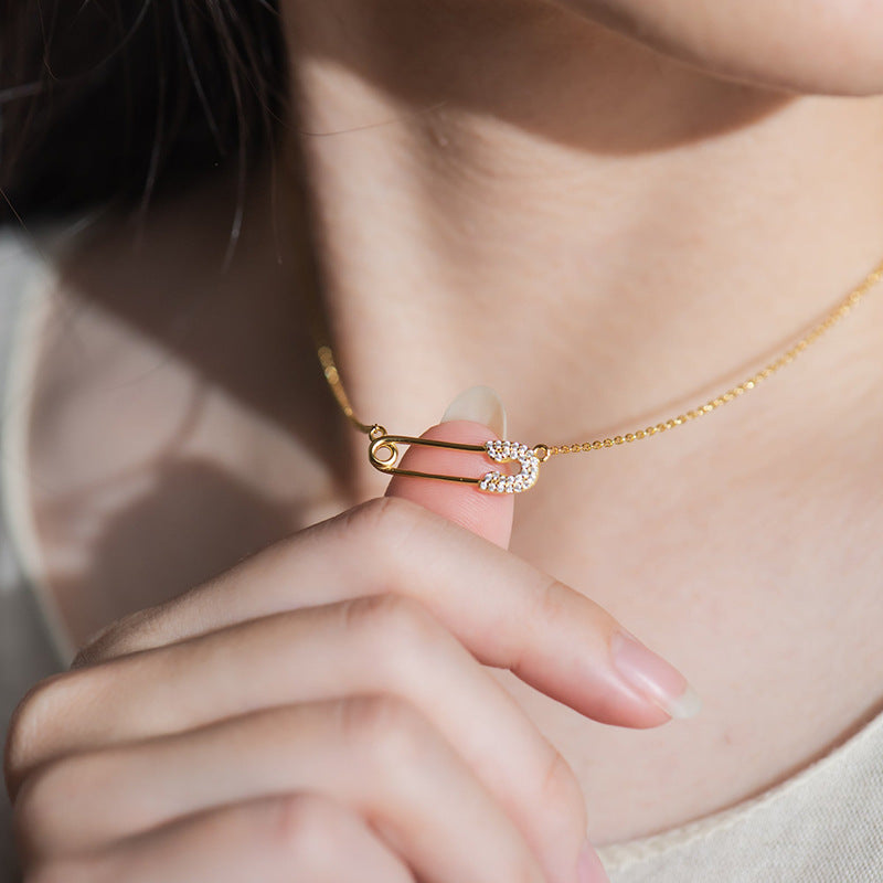 “Woman wearing minimalist silver safety pin necklace layered with simple chain”