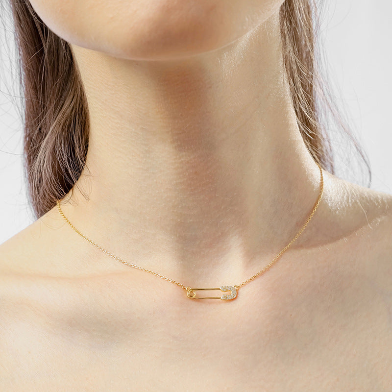 “Woman wearing minimalist silver safety pin necklace layered with simple chain”