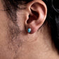 Close-up of an ear wearing a turquoise stud earring with dark hair and skin in the background.