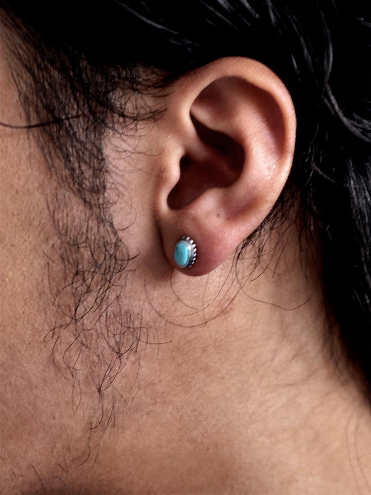 Close-up of an ear wearing a turquoise stud earring with dark hair and skin in the background.