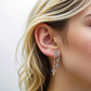 Close-up of a woman's ear wearing a S925 Sterling Silver Vermeil Naxos Illusion Earrings with dangling charms on a plain background
