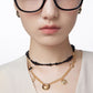 Person wearing a gold necklace with black beads on a plain background