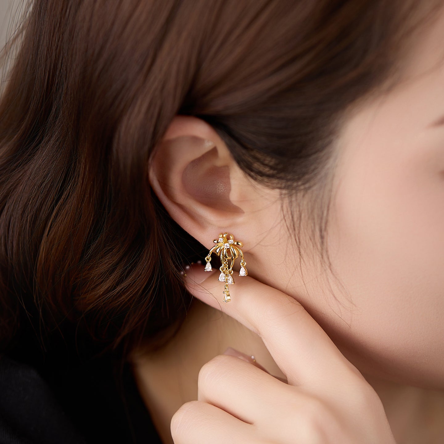 Close-up of a gold earring worn by a person with brown hair.