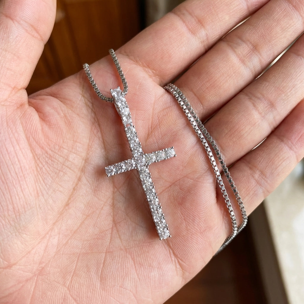 Silver cross pendant on a chain held in a hand