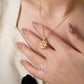 Gold necklace with a purple gemstone held by a hand against a neutral background