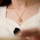 Gold necklace with a pendant worn by a person in a white sweater, with a blurred background.